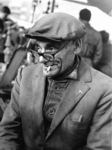 Fiera di Sinigaglia. Milano - Mercatino - Ritratto maschile - Anziano rigattiere con occhiali, cappello, sigaretta in bocca