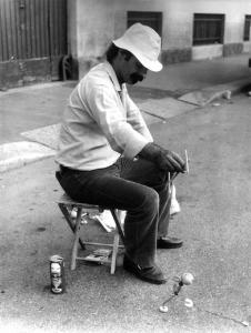 Fiera di Sinigaglia. Milano - Mercatino - Ritratto maschile - Uomo seduto su sgabello al lavoro - Ambulante artigiano - Lattina di birra