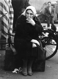Fiera di Sinigaglia. Milano - Mercatino - Ritratto femminile - Anziana rigattiere seduta su baule - Foulard in testa - Sigaretta