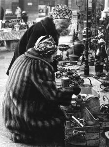 Fiera di Sinigaglia. Milano - Mercatino - Banco di un rigattiere - Donne con pelliccia e foulard in testa