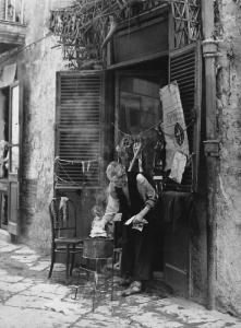 Napoli: Nei Bassi. Napoli - Vicoli - Anziano sulla porta di casa mette della carta su un braciere - Corno portafortuna