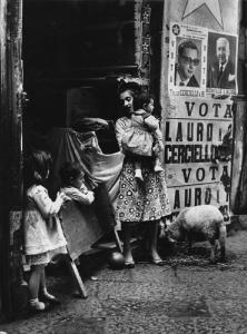 Napoli: Nei Bassi. Napoli - Vicoli - Donna con bambini sull'uscio di casa - Manifesti di propaganda politica elettorale - Pecora