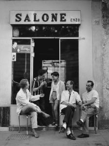 Napoli: Lavoro. Napoli - Vicoli - Ritratto di gruppo - Uomini seduti e due giovani in piedi sulla porta del salone del barbiere Enzo