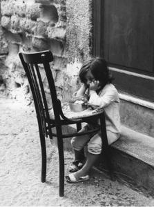 Napoli: Scugnizzi, passatempi. Napoli - Vicoli - Ritratto infantile - Bambina seduta su un gradino con sedia davanti - Pentola con cibo - Pranzo