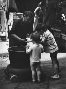 Napoli: Scugnizzi, passatempi/ Scene di vita varie. Napoli - Vicoli - Street food - Bambini davanti a un braciere, pentolone con anziana cuoca - Pannocchia di mais