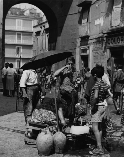 Napoli: Commercio. Napoli - Strada - Venditore ambulante di limonate: donna - Anziana con bicchiere in mano - Bambino - Ombrello