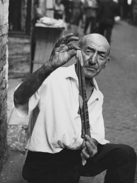 Napoli: Commercio. Napoli - Vicoli - Ritratto maschile - Venditore ambulante di calze: anziano - Paio di calzini in mano