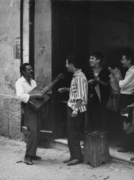 Napoli: Scene di vita varie. Napoli - Vicoli - Ritratto di gruppo - Uomo musicista con chitarra e ragazzi, sarti - Musica, canto