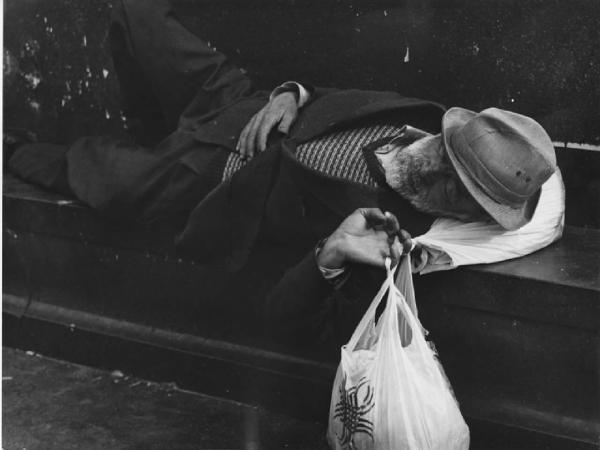 Piazza Duomo. Milano - Piazza del Duomo - Monumento a Vittorio Emanuele II - Ritratto maschile - Anziano senzatetto sdraiato con borsa in mano - Riposo