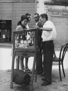 Napoli: Commercio. Napoli - Strada - Ritratto di gruppo - Venditore ambulante di orologi con clienti davanti alla vetrinetta: anziano - Banchetto
