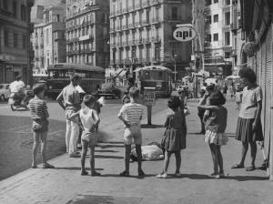 Napoli: Scene di vita varie. Napoli - Strada - Uomo sdraiato a terra circondato da bambini e ragazza - Pompa di benzina sullo sfondo