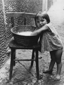 Napoli: Bimbi, soli. Napoli - Vicoli - Ritratto infantile - Bambina a piedi nudi con mani in un catino d'acqua su una sedia