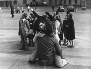 Piazza Duomo: Amore. Milano - Piazza del Duomo - Coppia di ragazzi sui gradini - Bacio, abbraccio - Gruppo di persone in visita guidata in secondo piano