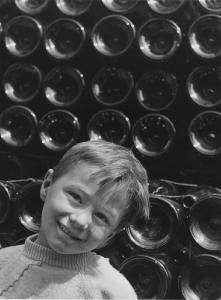 Lombardia. Ritratto infantile - Bambino con bottiglie vuote accatastate sullo sfondo