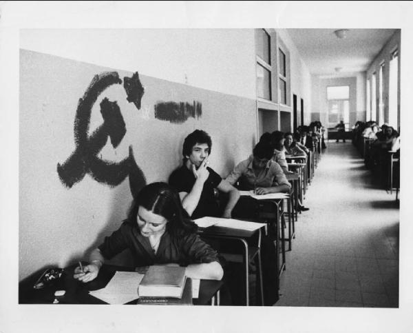 Scuola: esami di maturità. Milano (?) - Scuola superiore, corridoio - Esame di maturità - Gruppo di studenti ai banchi - Simbolo falce e martello sul muro
