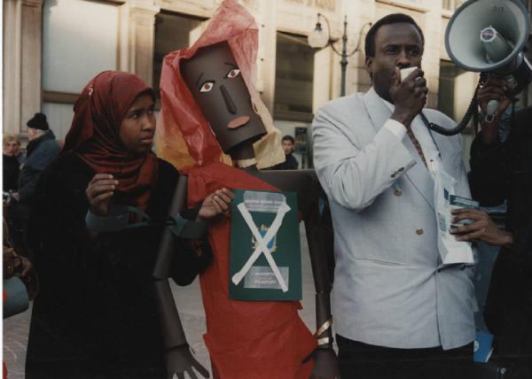 Manifestazione comunità somala. Milano - Manifestazione comunità somala - Coppia di manifestanti - Uomo con megafono, ragazza con manette di carta e manichino - Passaporto