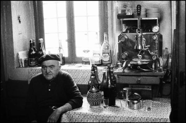 Milano - Via Pescara - "Osteria Ronchetto", interno - Ritratto maschile: uomo anziano con berretto seduto ad un tavolo - Macchina del caffè - Bottiglie - Finestra