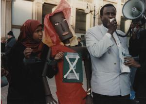 Manifestazione comunità somala. Milano - Manifestazione comunità somala - Coppia di manifestanti - Uomo con megafono, ragazza con manette di carta e manichino - Passaporto