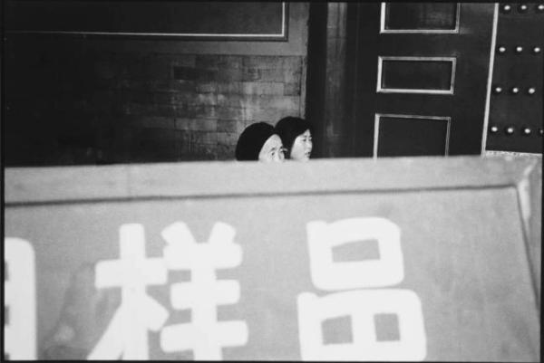 Anziana e giovane cinesi dietro a un cartellone