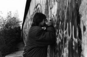 Berlino Ovest - ragazzo fotografa la parte est della città attraverso un buco del muro