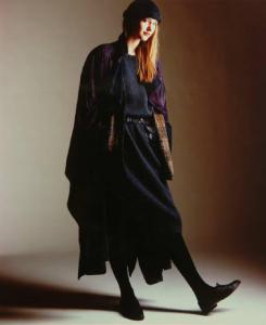 Campagna pubblicitaria per Trussardi Donna - Modella a figura intera: cappotto scamosciato viola su vestito lungo di maglia, stringate in pelle e cappello