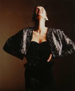 Campagna pubblicitaria per Trussardi Donna - Modella con mani sui fianchi e viso rivolto all'insù: mantellina fantasia, abito di velluto con scollo a cuore