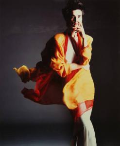 Campagna pubblicitaria per Trussardi Donna - Modella con braccia incrociate e mano sul viso: spolverino svolazzante giallo e rosso