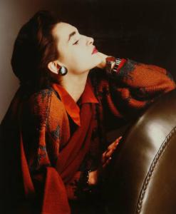 Campagna pubblicitaria per Trussardi Donna - Modella di profilo: maglione rosso e gigio, camicia rossa - Orecchini, bracciale e orologio argentati - Poltrona di pelle