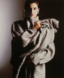 Campagna pubblicitaria per Trussardi Donna - Modella con braccia avvolte al busto: robe-manteau di pelle plissettata grigia - Orecchini metallici