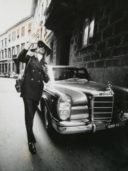 Campagna fotografica per "Vogue" - la modella Isa Stoppi indossa un tailleur pantalone gessato con occhialoni da sole e cappello - posa accanto a un'automobile Mercedes