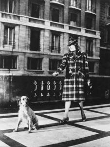 Modella indossa un cappotto scozzese e cappellino - tiene al guinzaglio un cane