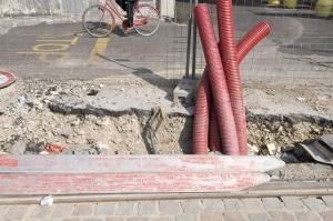 Tramsformazione. Milano - Cinisello Balsamo - Cantiere della metrotranvia - Rotaia - Tubi di gomma rossa nello scavo - Persona in bicicletta (particolare delle gambe)