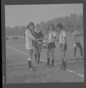 Ritratto di gruppo maschile - Torneo di calcio 1973 - Saluto tra i capitani delle due squadre con scambio di gagliardetto e coppa.