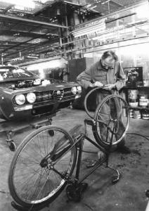Fabbrica Alfa Romeo di Arese - Interno - Operaio ripara la gomma di una bicicletta - Automobile in costruzione