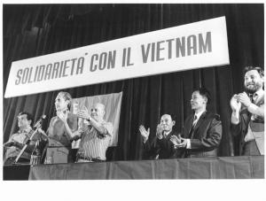 Teatro Odeon - Interno - Manifestazione in solidarietà con il Vietnam - Palco - Tavolo della presidenza con oratori che applaudono, tra i quali Leonardo Banfi, delegazione vietnamita, Sergio Soave - Bandiera - Parola d'ordine