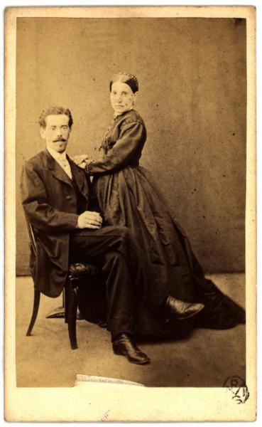 Ritratto di coppia - Uomo seduto e donna in piedi con la mano sulla spalla di lui
