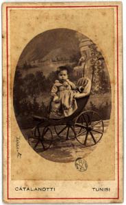 Ritratto infantile - Bambino in piedi su una carrozzina davanti a un fondale dipinto