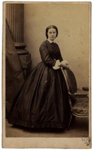 Ritratto femminile - Donna in abito scuro, in piedi accanto a una sedia
