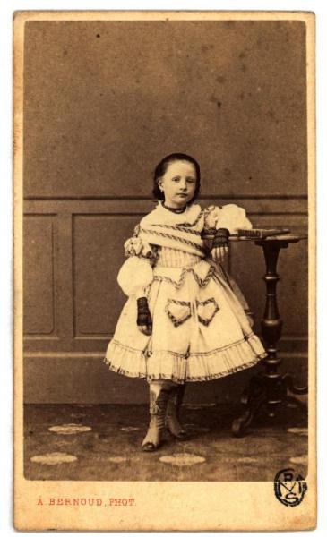 Ritratto infantile - Bambina in abito con tasche ricamate, stivaletti con lacci e mezzi guanti