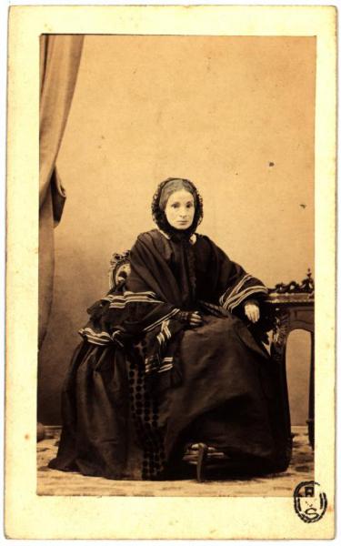 Ritratto femminile - Donna in abito scuro con cuffia seduta accanto a un tavolo