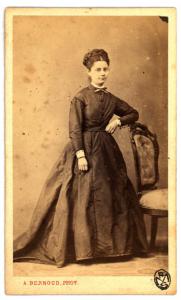 Ritratto femminile - Donna con acconciatura raccolta, in piedi accanto a una sedia