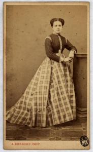 Ritratto femminile - Giovane donna con gonna a scacchi, in piedi appoggiata a un piedistallo.