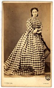 Ritratto femminile - Donna in abito a quadri in piedi con le braccia appoggiate sullo schienale di una sedia