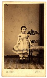 Ritratto infantile - Bambina in piedi accanto a una sedia