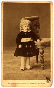 Ritratto infantile - Bambina in piedi accanto a una poltrona