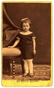Ritratto infantile - Bambina in piedi accanto a una poltroncina