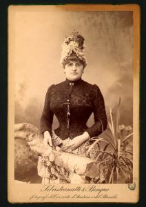 Ritratto femminile - Donna con occhiali e cappello, in piedi dietro un finto tronco