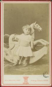 Ritratto infantile - Bambina in piedi davanti a un cavallo a dondolo