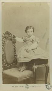 Ritratto infantile - Bambina seduta su uno sgabello con i piedi appoggiati su una sedia
