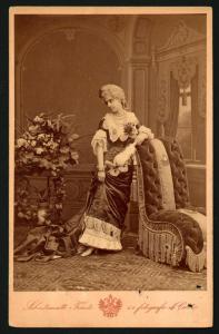 Ritratto femminile - Donna in abito da sera (forse un costume) in piedi appoggiata a una poltrona.
